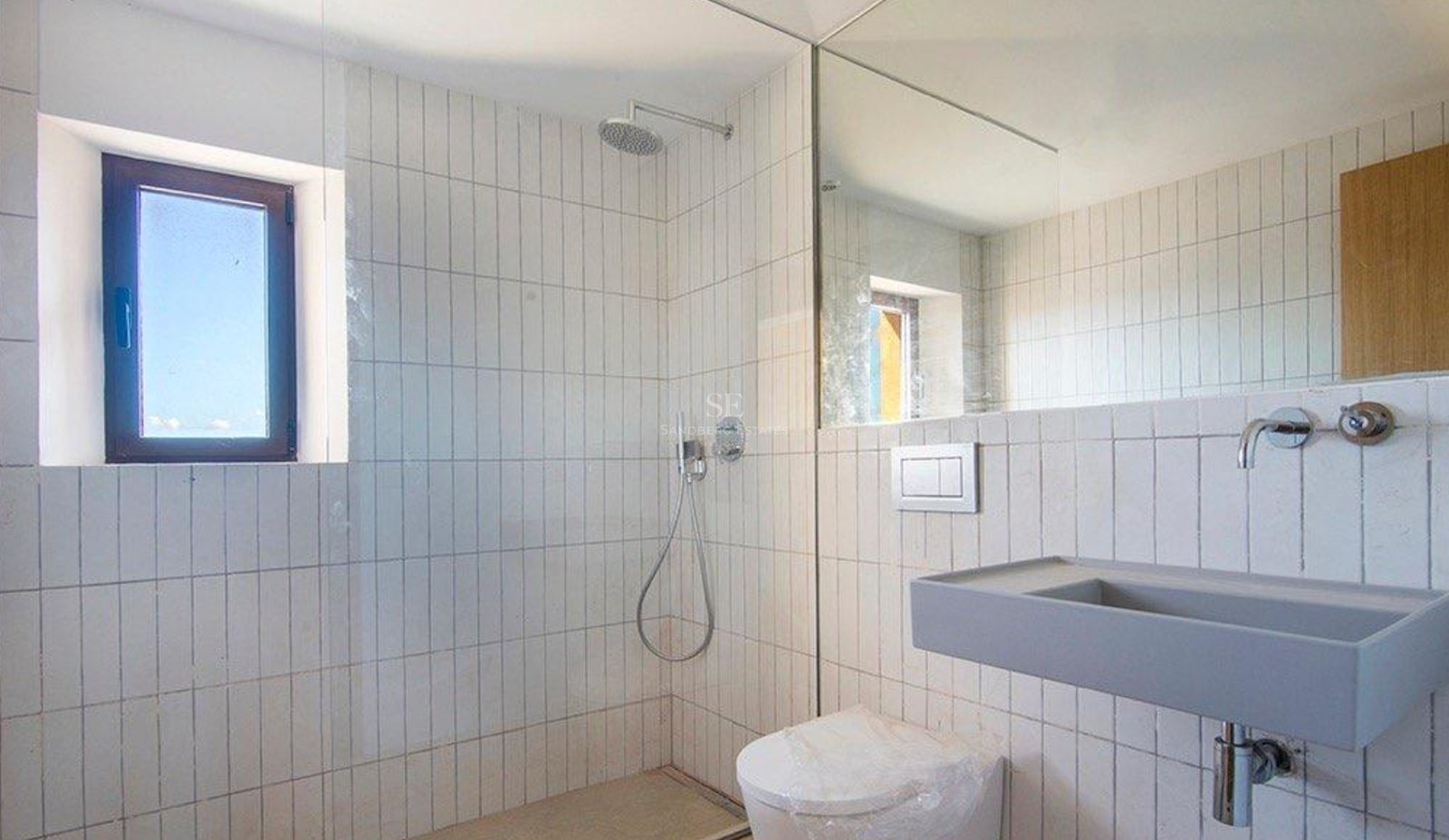 A modern bathroom with white vertical tiles, a walk-in shower, a grey floating sink, and a large wall mirror.