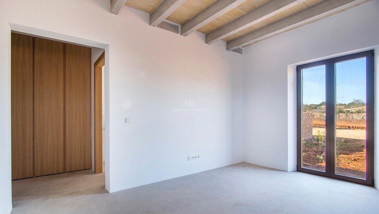 Empty bedroom featuring white walls, exposed wooden ceiling beams, built-in oak wardrobes, and a glass door to the exterior.