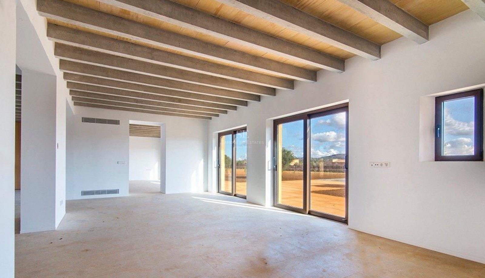 Spacious unfurnished living room featuring exposed ceiling beams, large sliding glass doors, and light stone flooring.