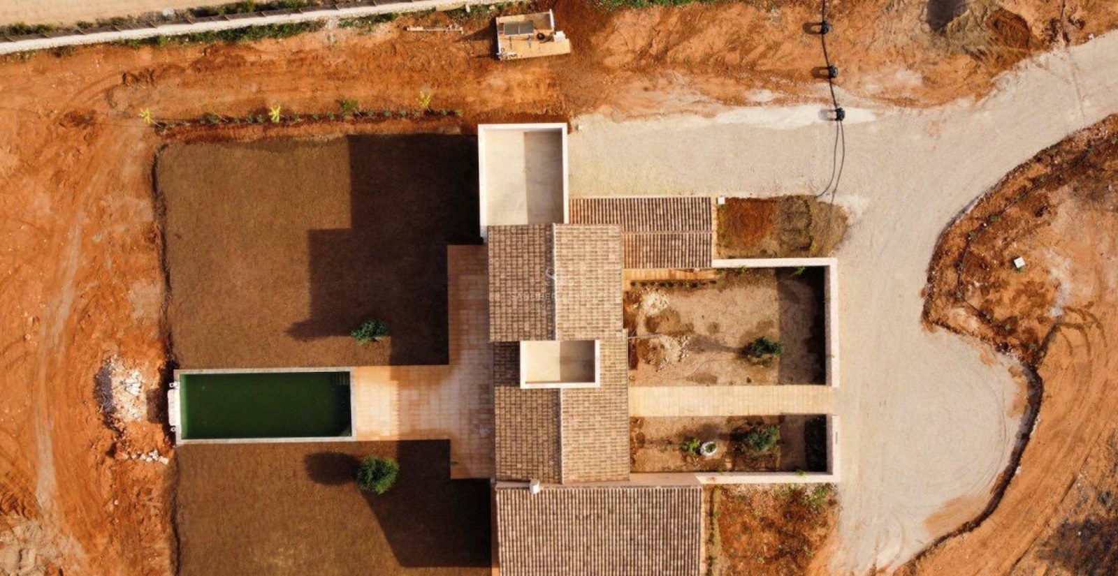 Top-down drone shot of a modern villa featuring tiled roofs, a rectangular pool, and courtyards under development.
