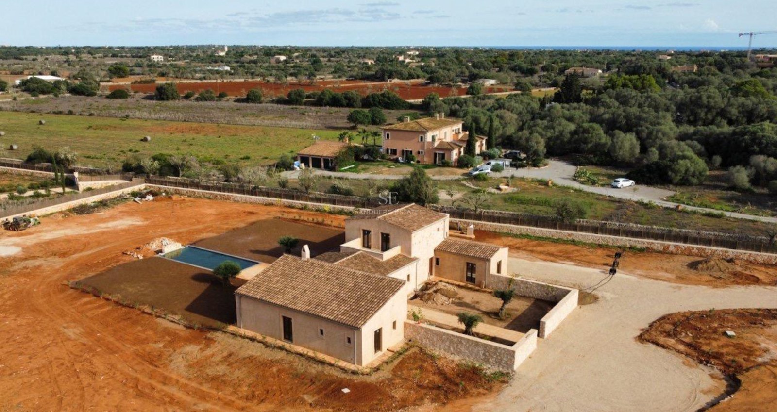 Aerial view of a large traditional Mallorcan villa with a swimming pool and stone walls under a clear sky.