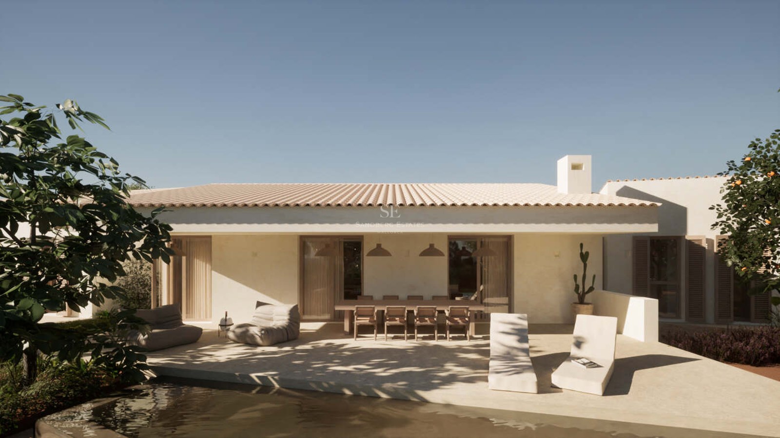 White plastered terrace featuring a long wooden dining table, lounge seating, and pool edge under a clear sky.