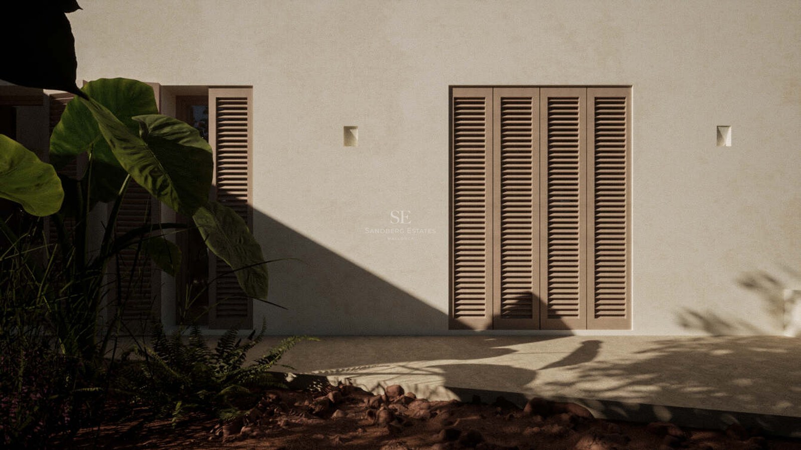 Sand-toned stucco exterior wall featuring closed louvered shutters and tropical foliage in the foreground shadows.