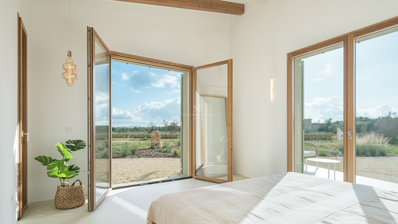 Bright bedroom featuring large wood-framed glass doors opening onto a Mediterranean landscape with olive trees.
