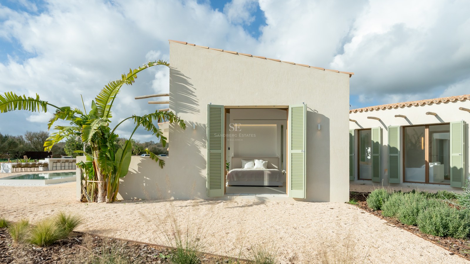 Exterior view of a minimalist sand-colored villa with sage green shutters opening into a bright master bedroom.