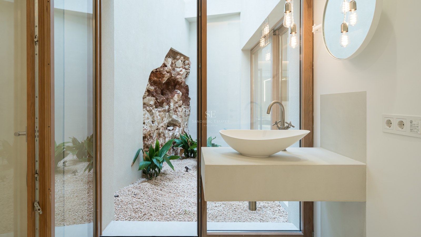 Modern vessel sink on a floating vanity looking through a glass wall at an internal courtyard with a natural stone feature.