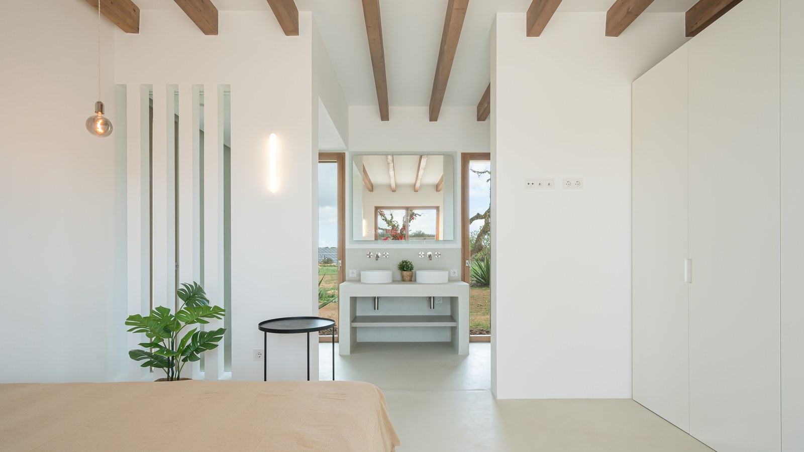 Minimalist master bedroom featuring white walls, exposed wooden beams, and an integrated ensuite vanity area.