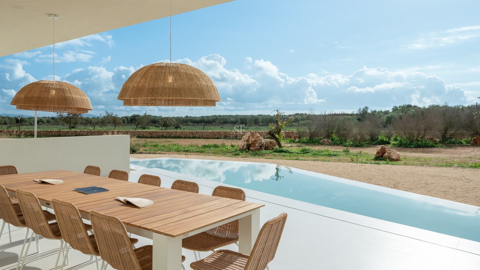 Modern wooden dining table and wicker chairs under a covered terrace next to a pool and rural landscape.