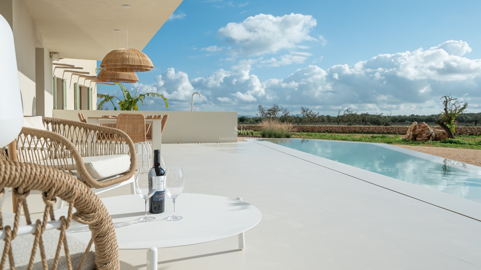 Luxury terrace with white microcement flooring, infinity pool, and woven furniture overlooking a Mediterranean landscape.