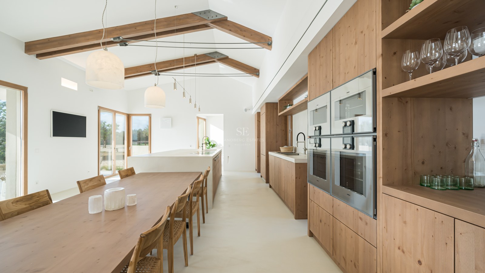 Bright open-plan kitchen and dining area with high vaulted ceilings, exposed wooden beams, and natural oak cabinetry.