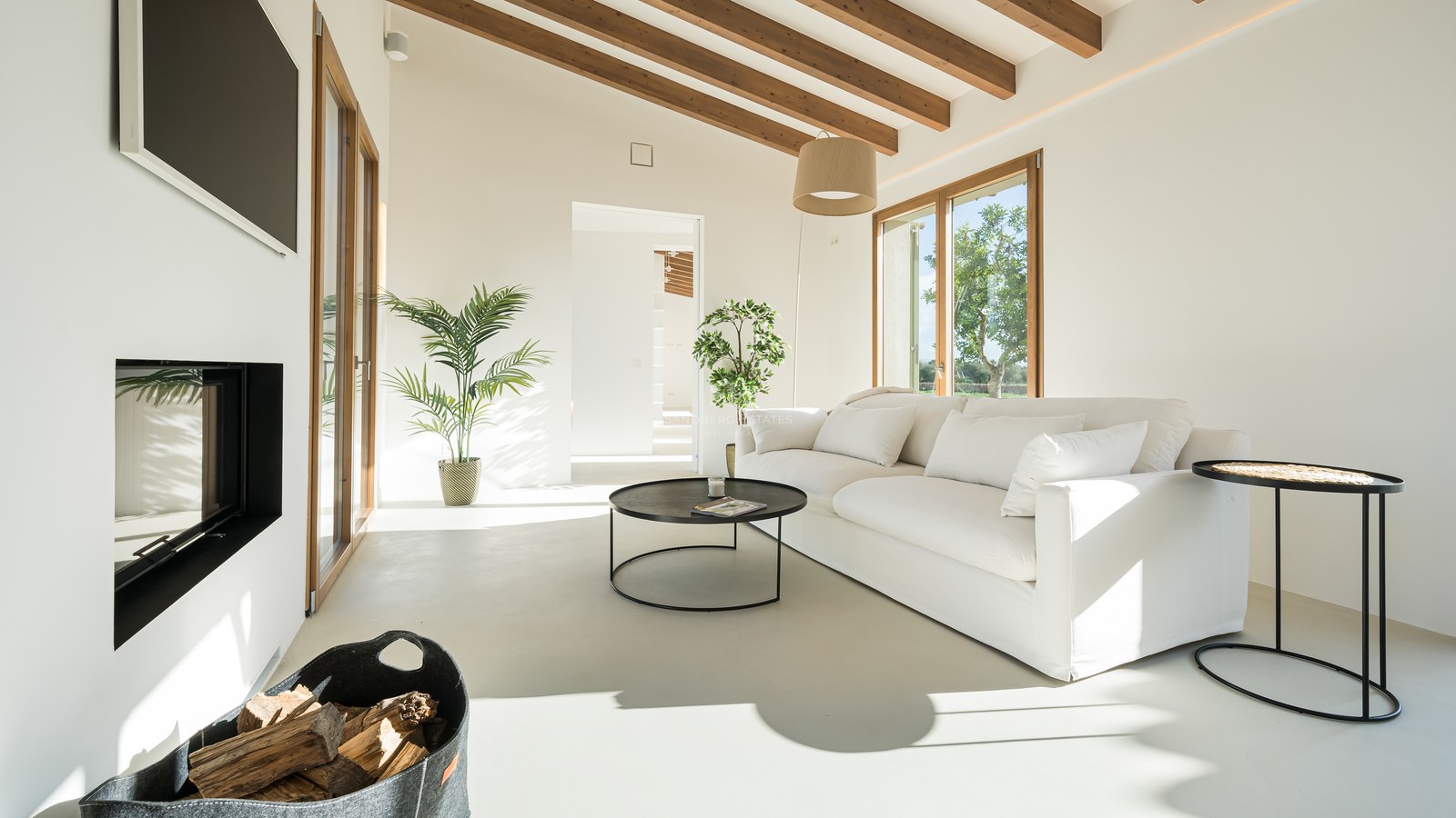 Minimalist living room with white sofa, wooden ceiling beams, modern fireplace, and floor-to-ceiling windows.