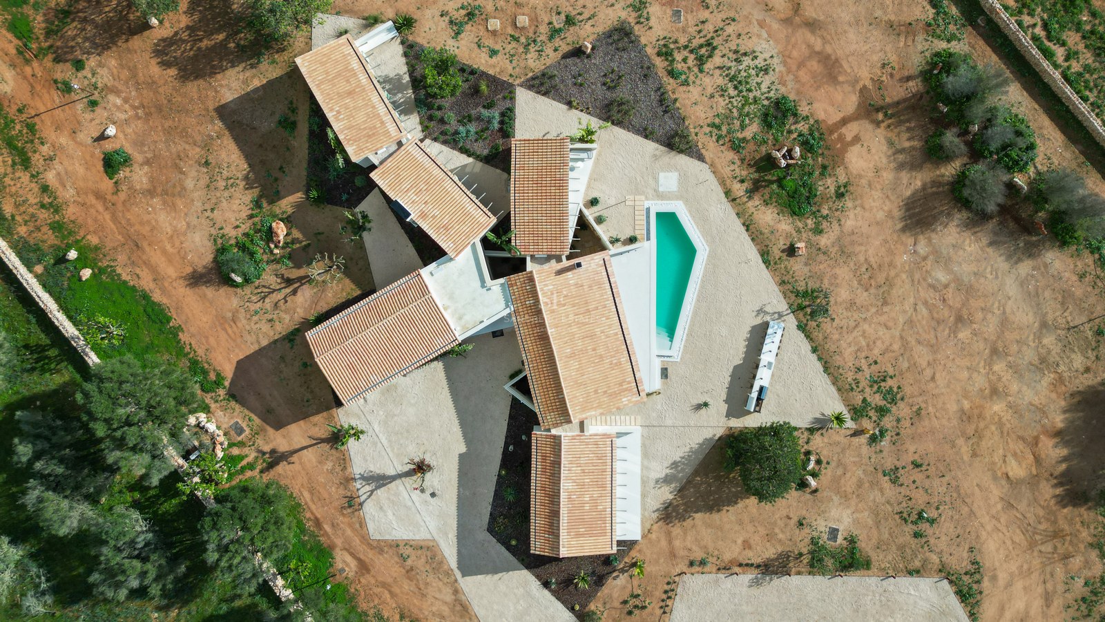Birds-eye view of a modern villa with terracotta roofs and a turquoise pool set in a natural landscape.