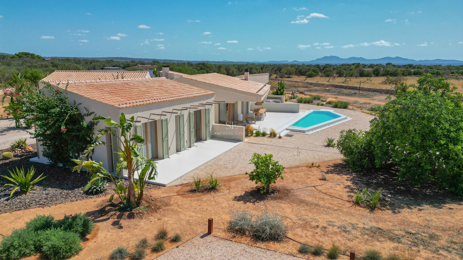 Aerial view of a modern single-story villa with terracotta roof, sage green shutters, and a geometric swimming pool.