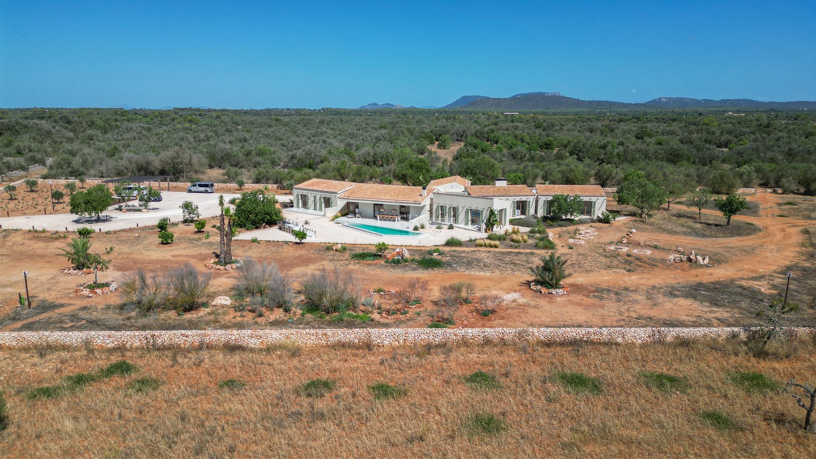 Aerial view of a modern white finca with terracotta roof and swimming pool surrounded by vast rural landscape.