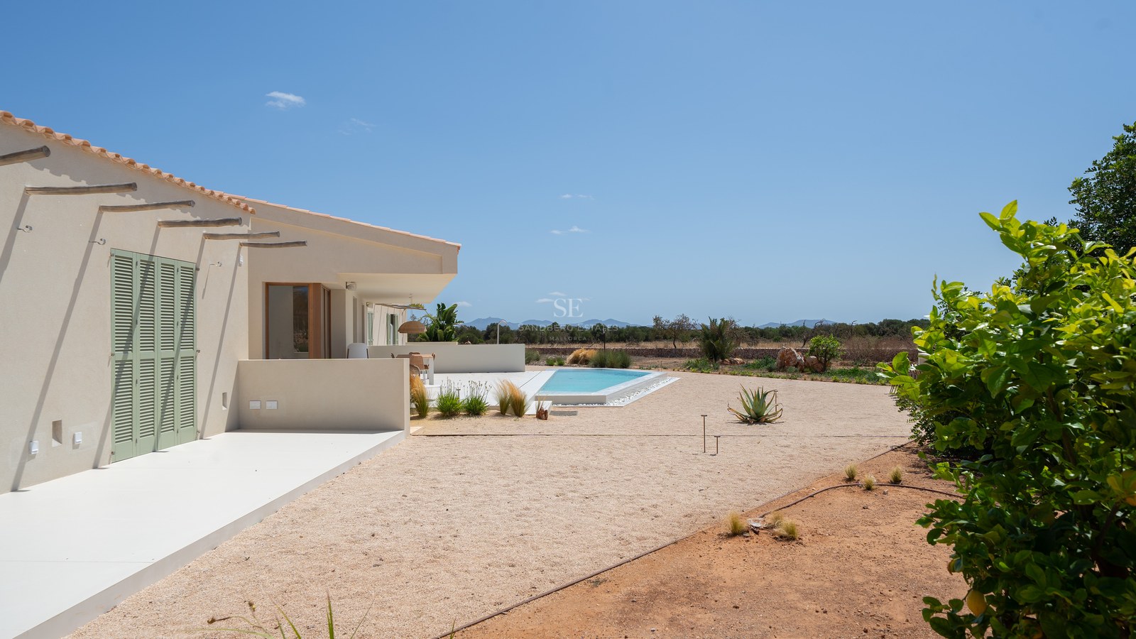 Modern beige villa with green shutters, a turquoise pool, and mountain views under a clear blue sky in Mallorca.