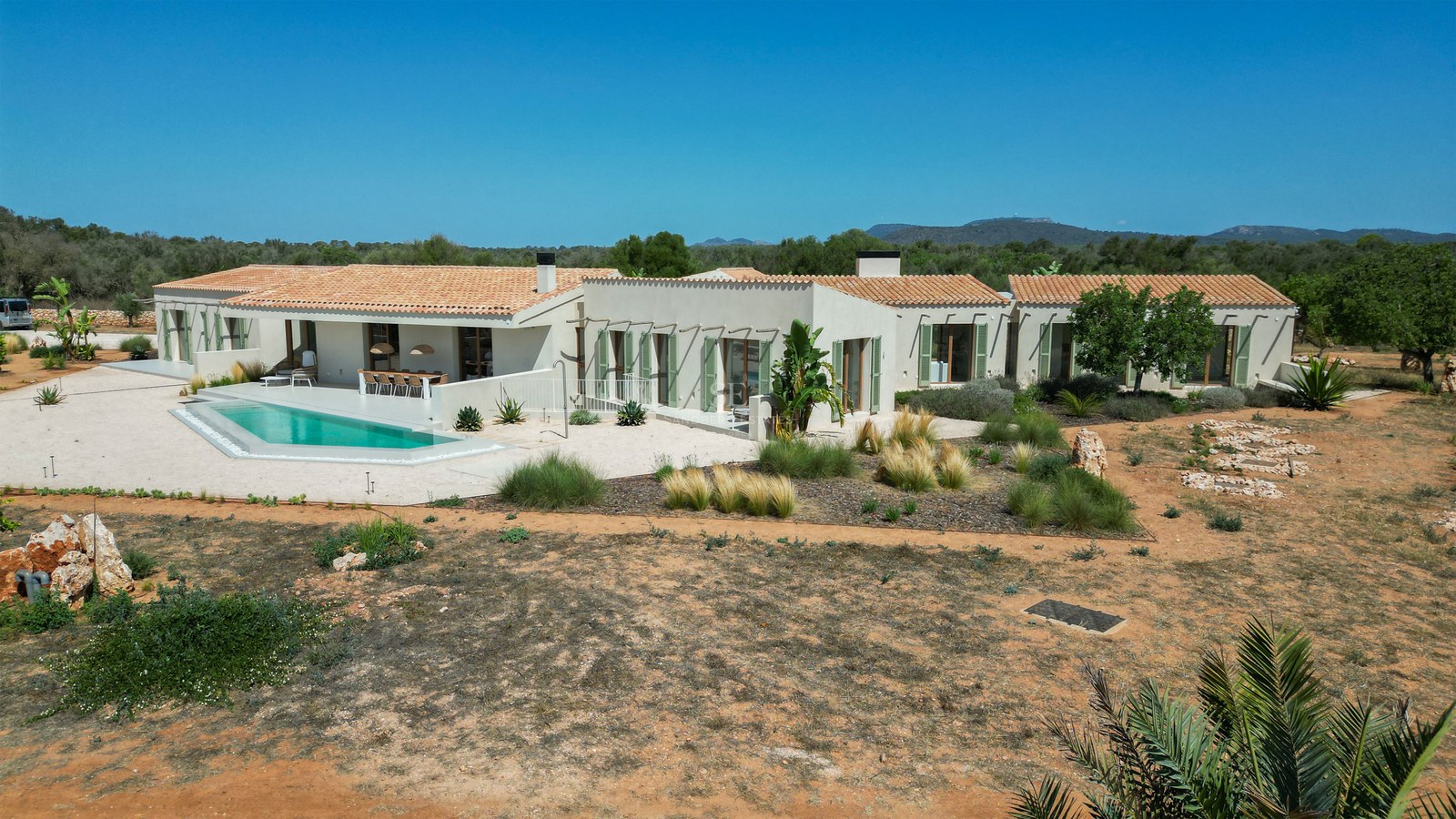 Aerial view of a luxury single-story villa with a pool, terracotta roof, and green shutters in a desert landscape.