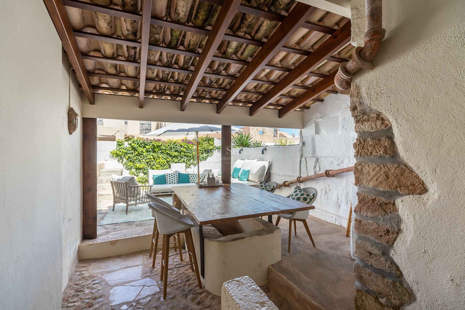 Überdachte mediterrane Terrasse mit großem Holztisch, Sichtbalken und hellem Außen-Loungebereich.