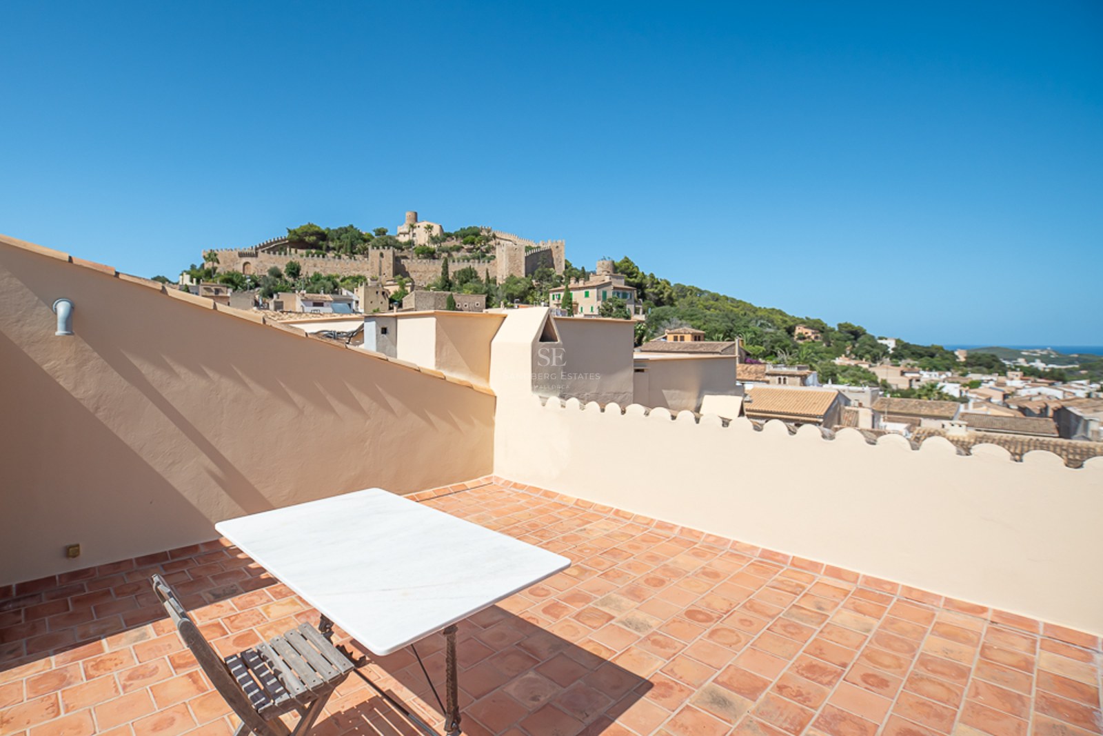 Dachterrasse mit Terrakottafliesen und Marmortisch, mit Blick auf eine historische Burg auf einem grünen Hügel.