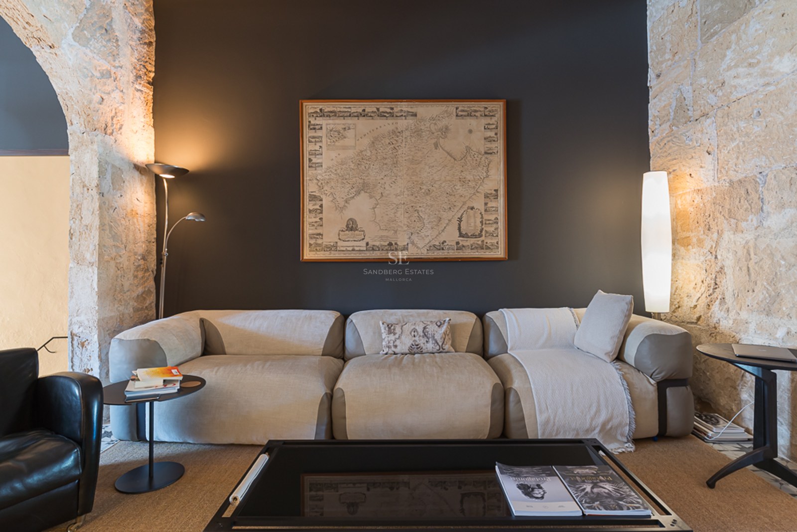 Modernes beiges Sofa vor anthrazitfarbener Wand mit Mallorca-Karte und freigelegten Natursteinbögen.