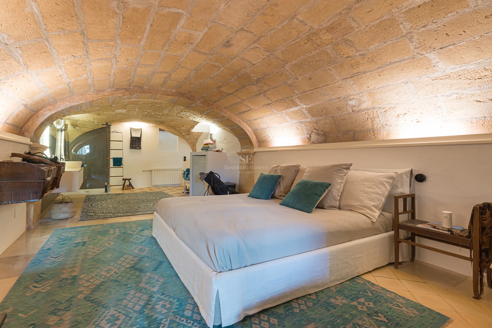 Schlafzimmer mit Sandsteingewölbe, weißen Wänden, türkisfarbenen Teppichen und modernem Bett.