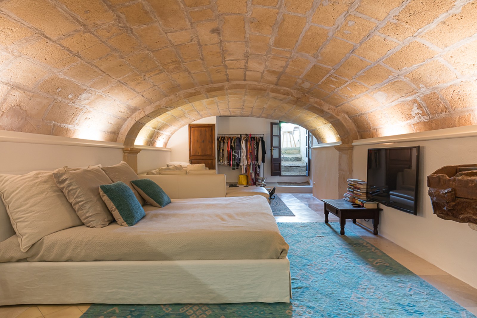 Schlafzimmer mit niedrigem Sandsteingewölbe, großem Bett mit türkisfarbenen Kissen und indirekter Beleuchtung.