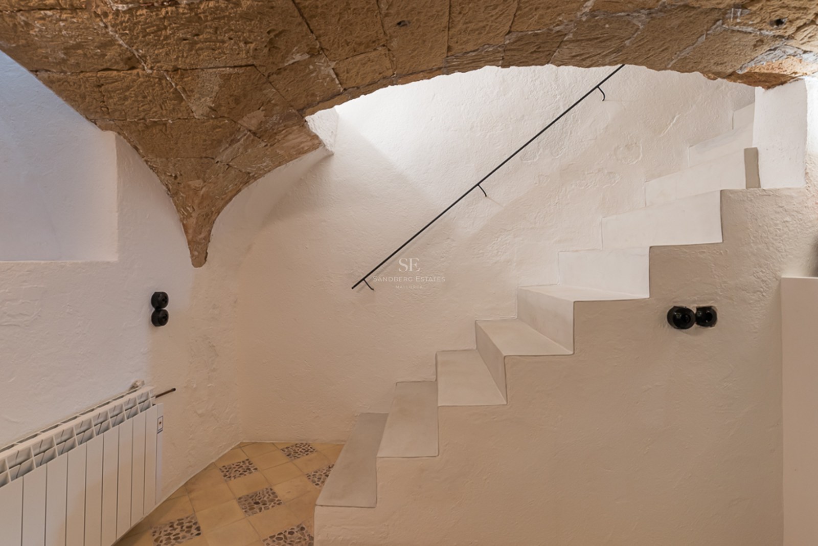 Minimalistische weiße Treppe unter einem Natursteinbogen in einem renovierten Stadthaus auf Mallorca.