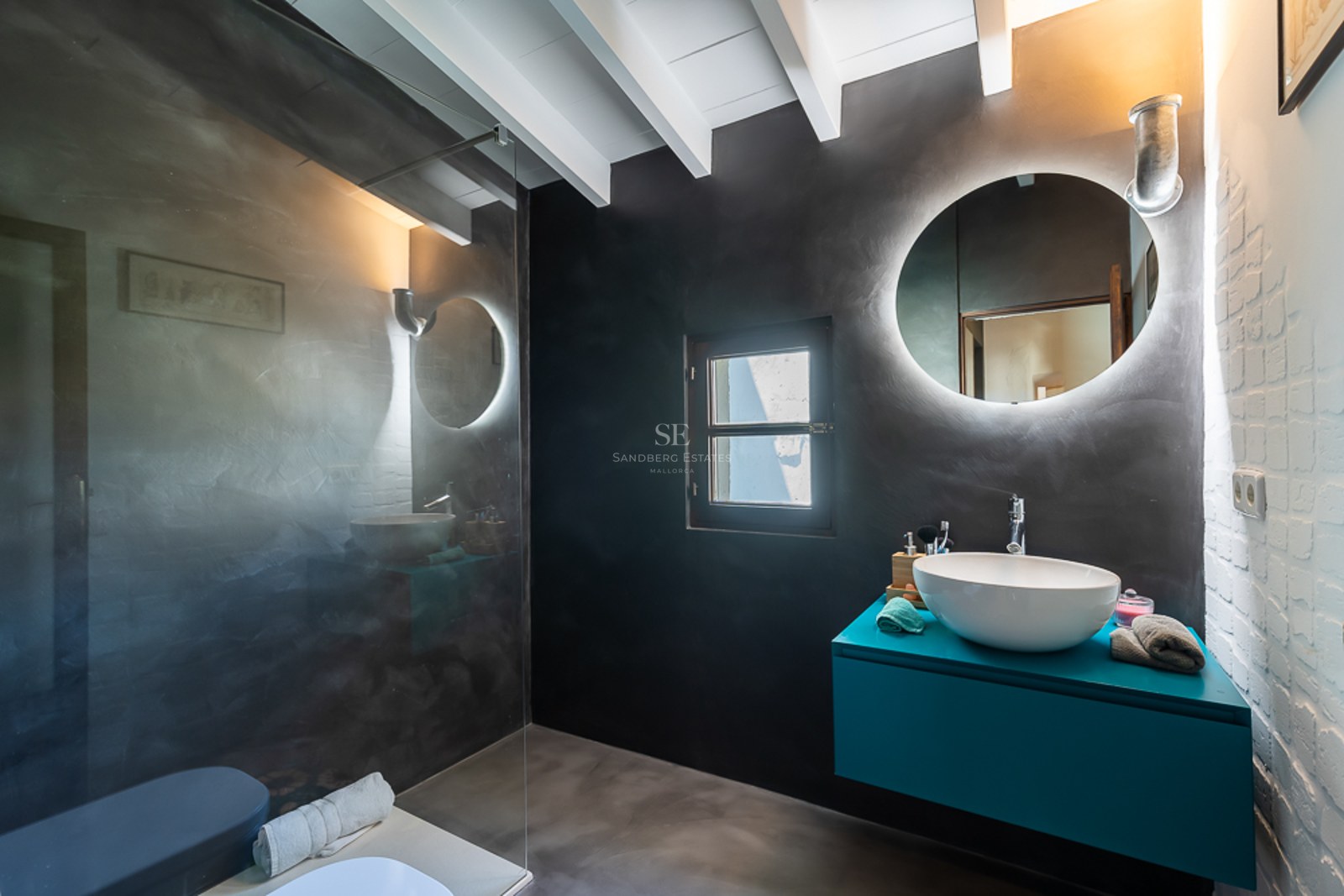 Modernes Badezimmer mit anthrazitfarbenen Mikrozementwänden, türkisblauem Waschtisch und hinterleuchtetem Rundspiegel.