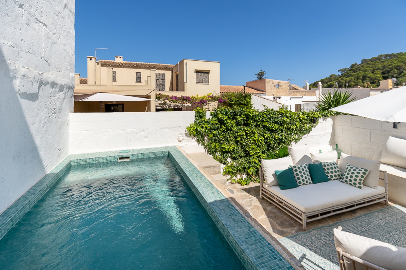 Privater türkisfarbener Pool in einem Innenhof mit weiß getünchten Wänden, Steinboden und Loungemöbeln.
