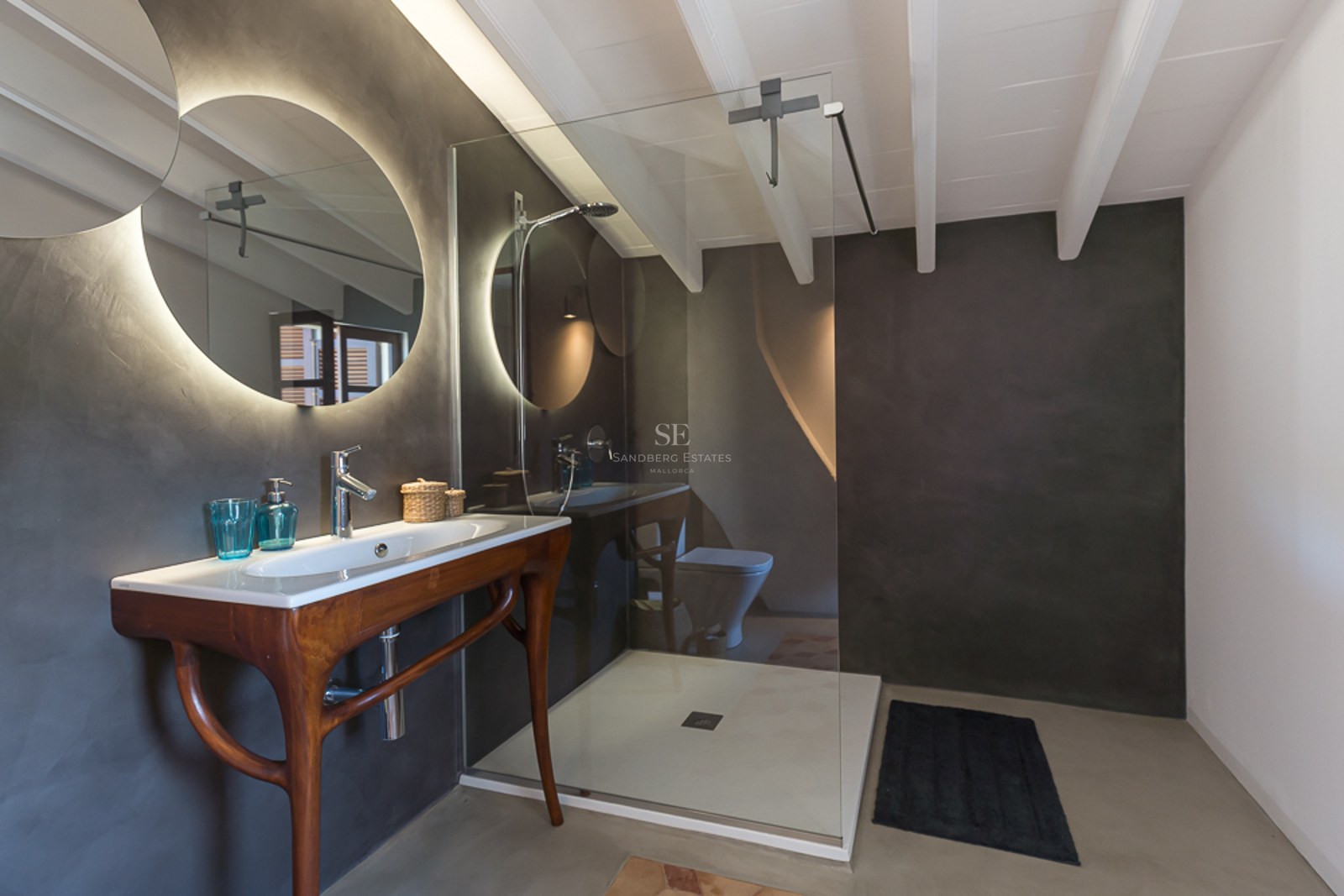 Modernes Badezimmer mit dunkelgrauen Mikrozementwänden, rundem beleuchtetem Spiegel und Holzwaschtisch.