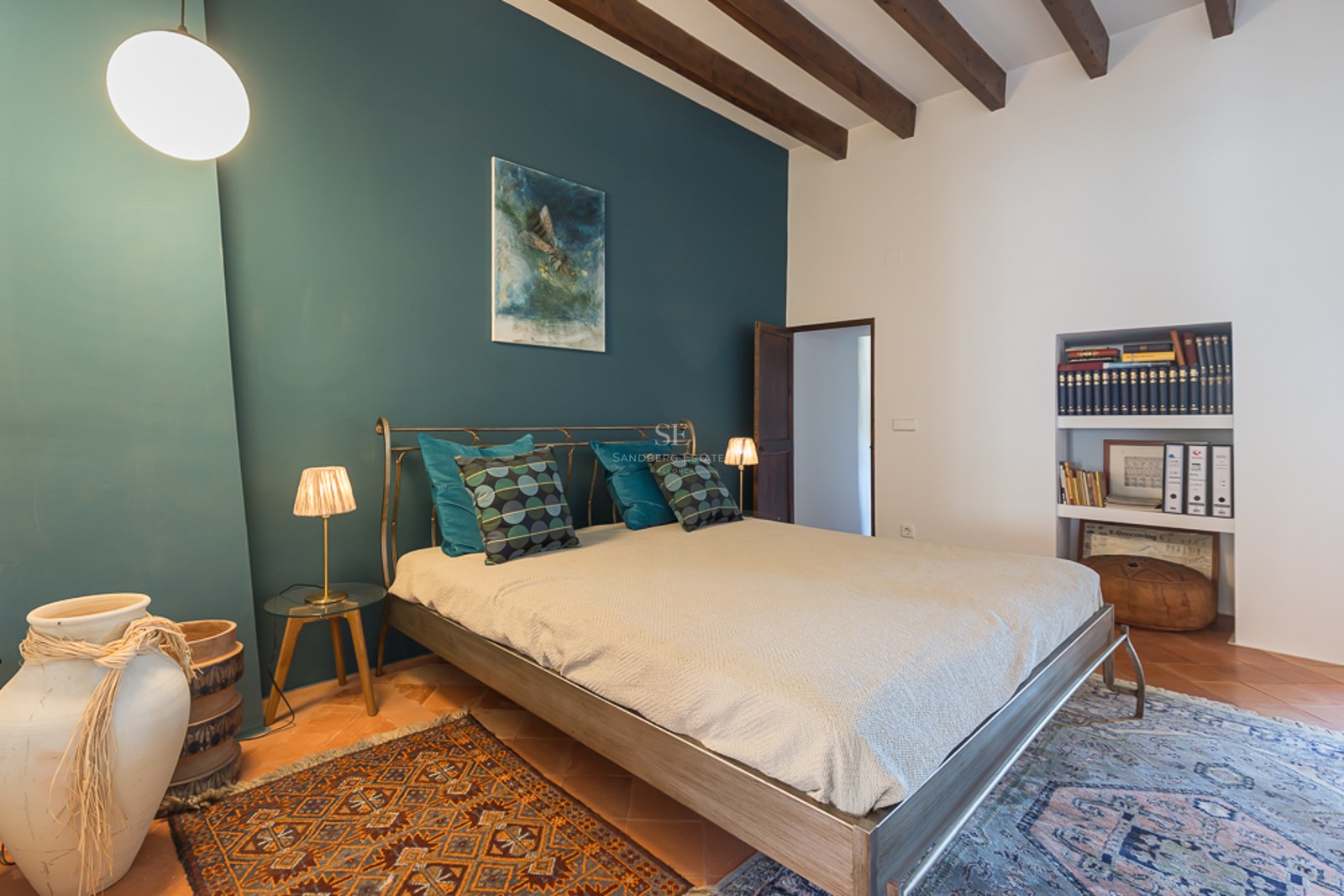 Schlafzimmer mit petrolfarbener Wand, Holzbalkendecke, Terrakottaboden und Metallbett.