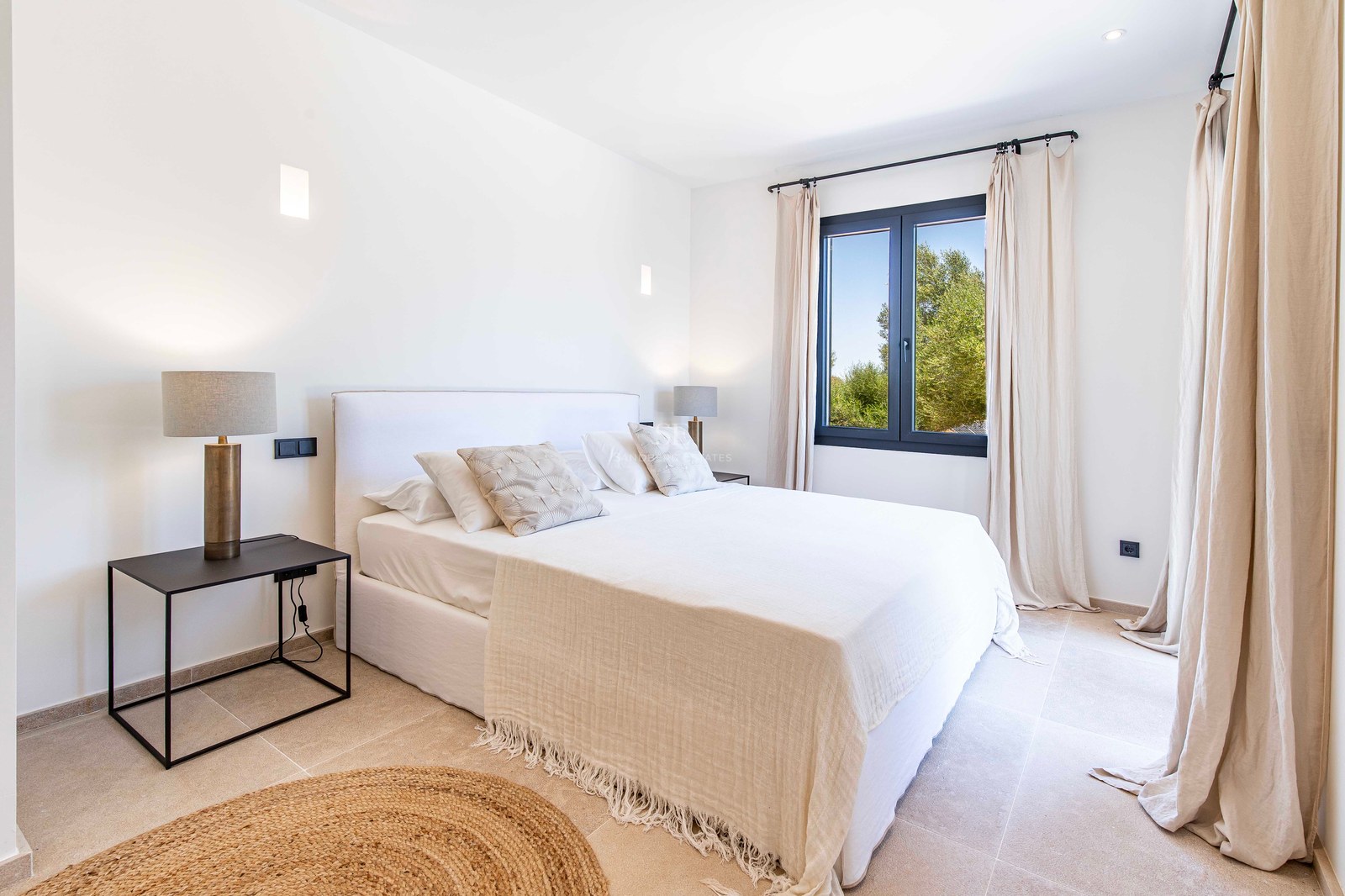 Chambre lumineuse avec lit double, sol en pierre naturelle, tapis en jute et vue sur les arbres.