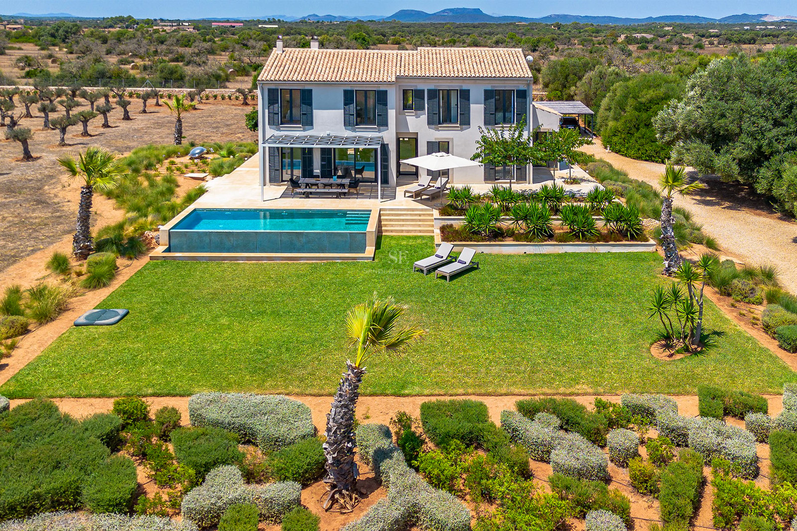 Vue aérienne d'une villa gris clair avec toit en terre cuite, piscine à bordement et grande pelouse à Majorque.