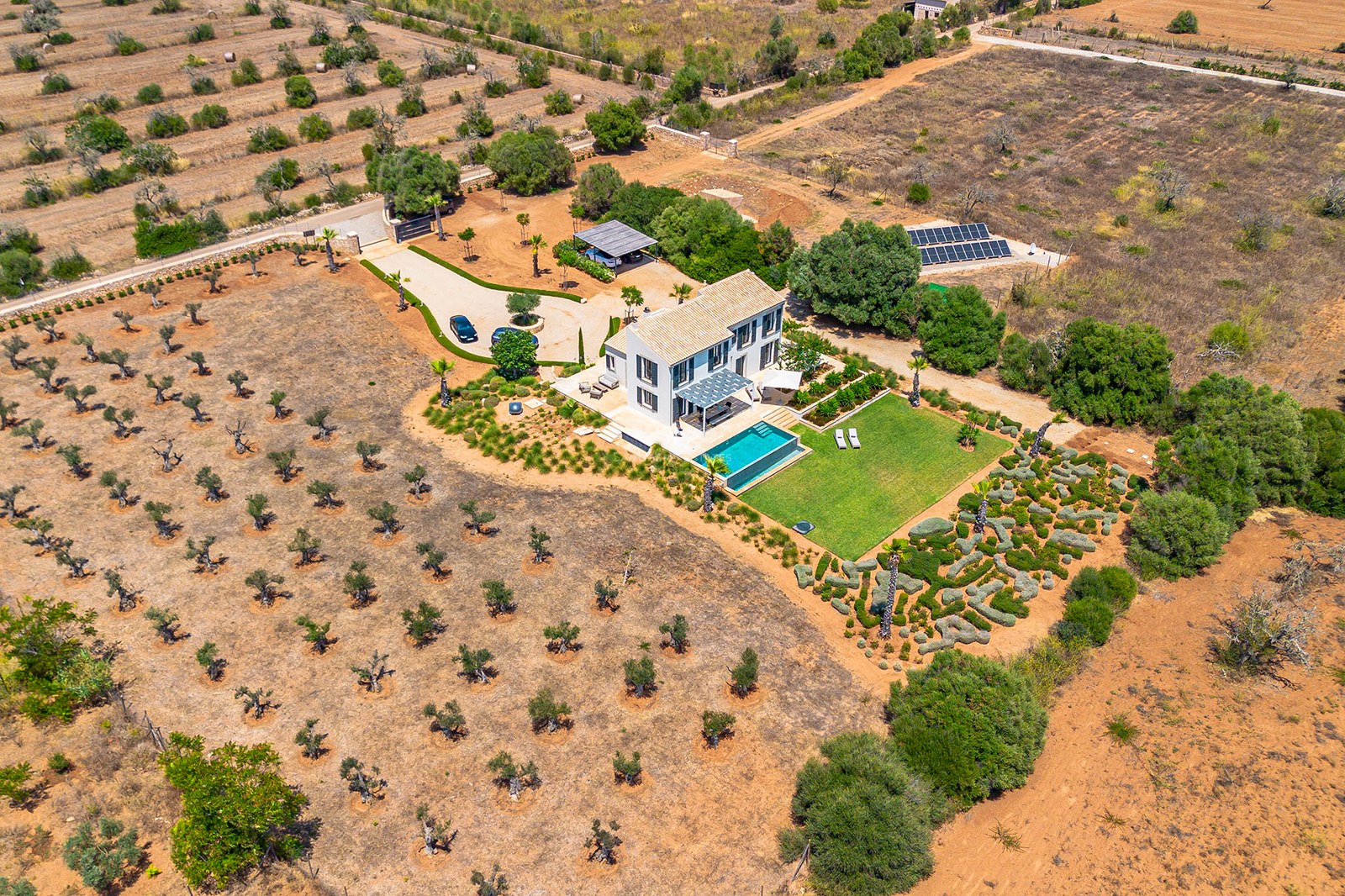 Vue par drone d'une villa contemporaine avec piscine, oliveraies et panneaux solaires sur un vaste terrain.