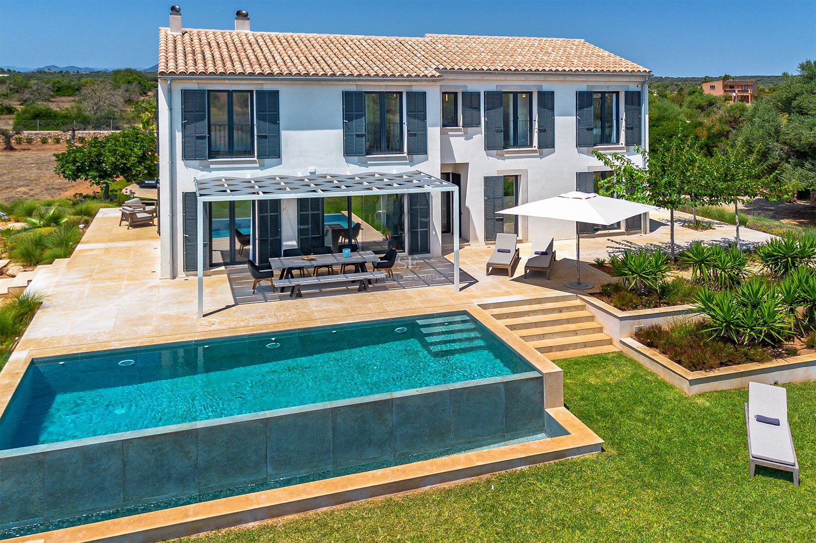 Vue extérieure d'une villa blanche avec piscine rectangulaire, terrasse en pierre et pergola moderne.