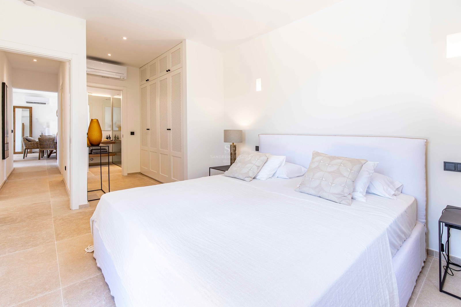 Chambre principale lumineuse avec linge de lit blanc, armoires encastrées et vue sur la salle de bains attenante.