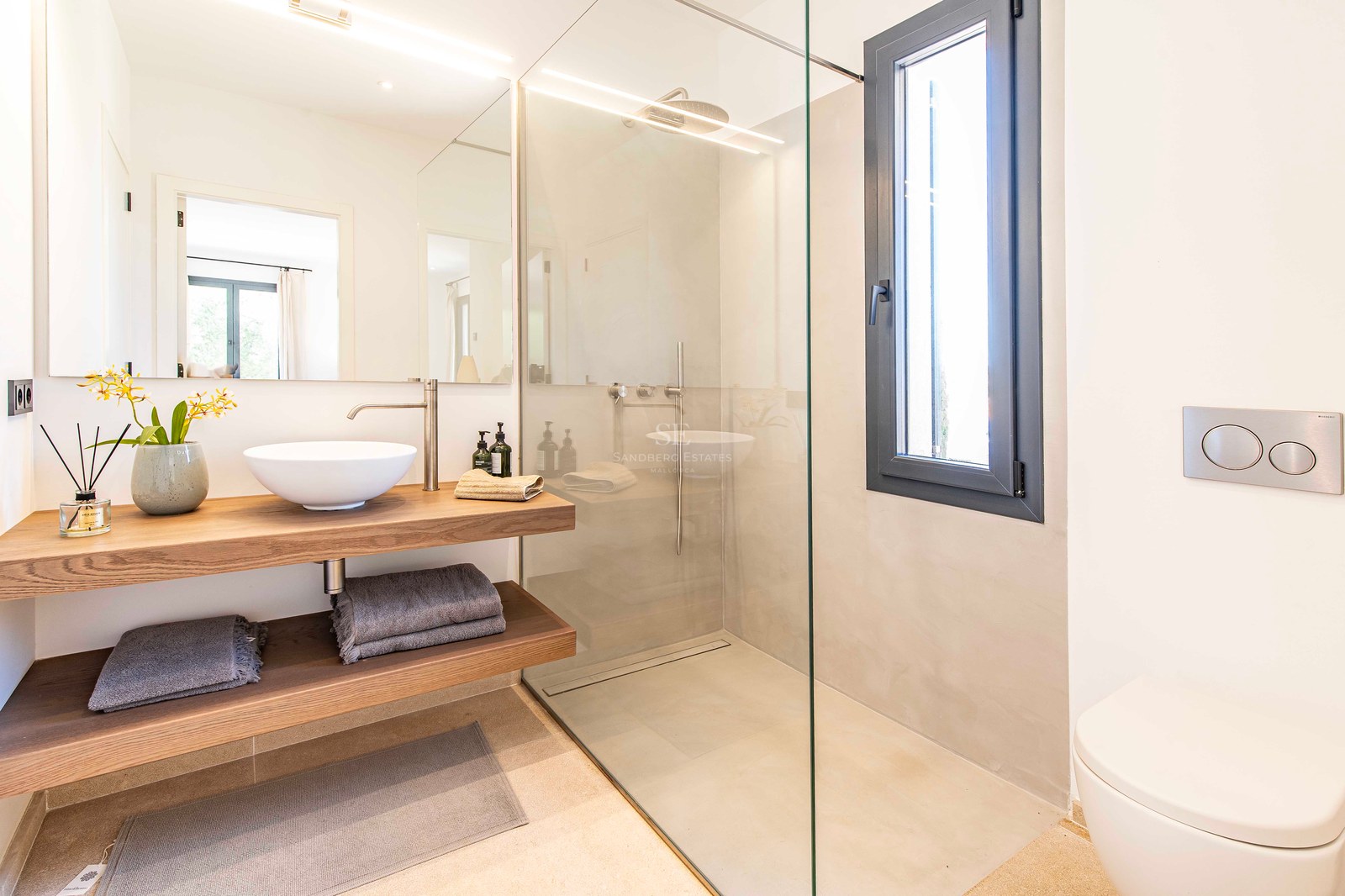 Salle de bains moderne avec douche vitrée, vasque à poser sur plan en chêne et grand miroir lumineux.