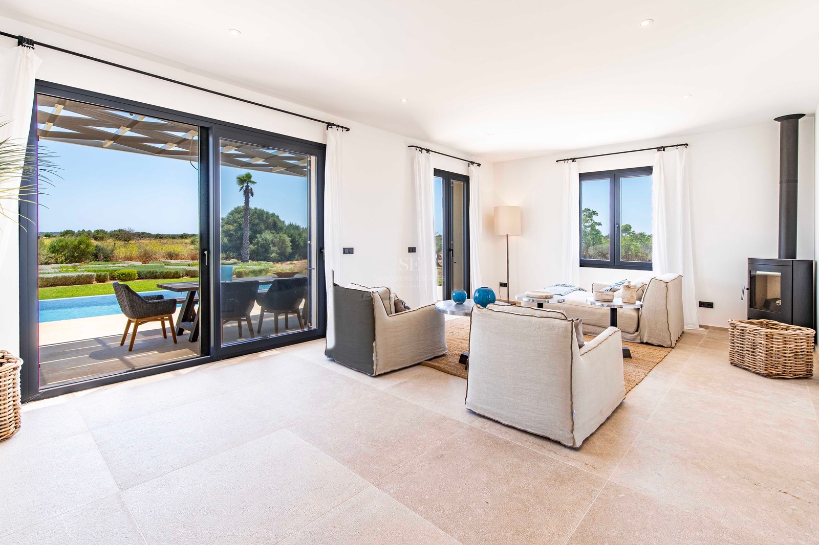 Salon lumineux avec baies vitrées s'ouvrant sur une terrasse avec piscine et jardin sous un ciel bleu.