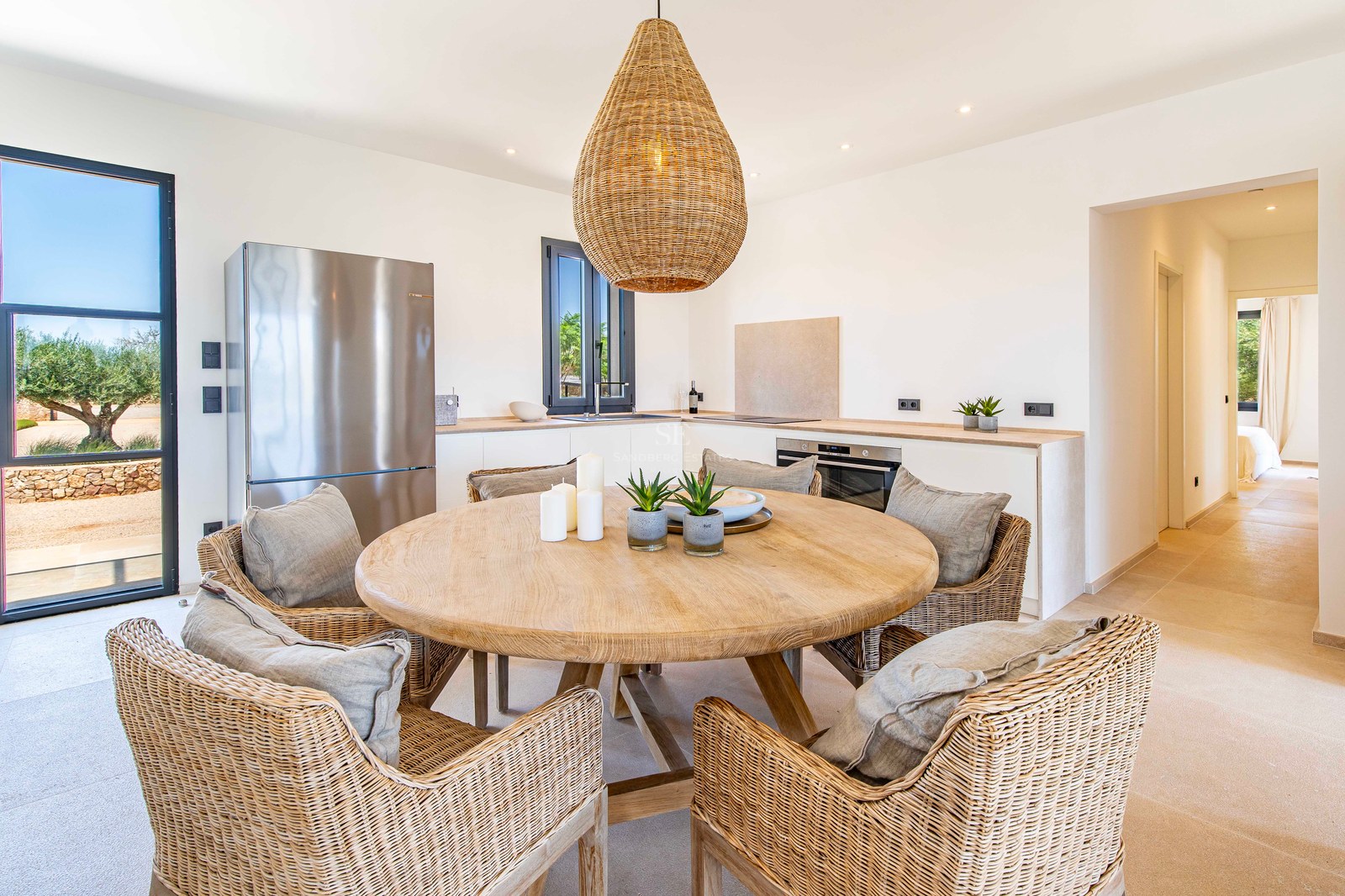 Table à manger ronde en bois avec six chaises en osier et suspension tressée dans une cuisine lumineuse.