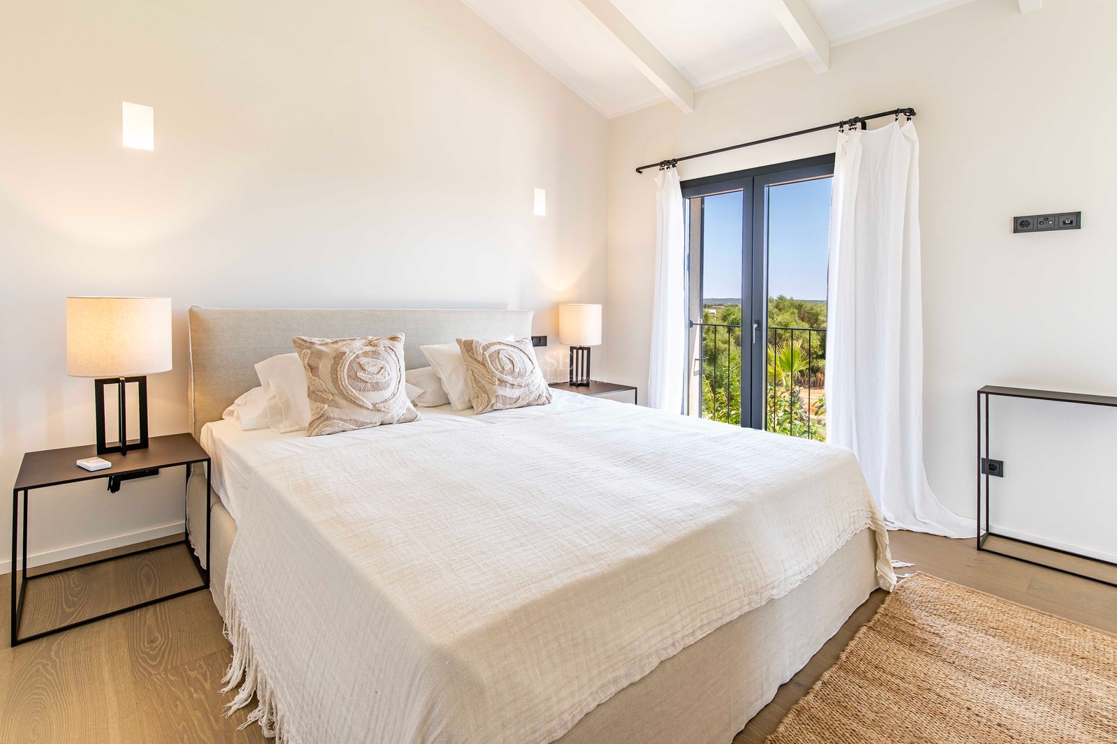 Chambre lumineuse avec draps blancs, parquet en bois, plafond à poutres et porte vitrée donnant sur la verdure.