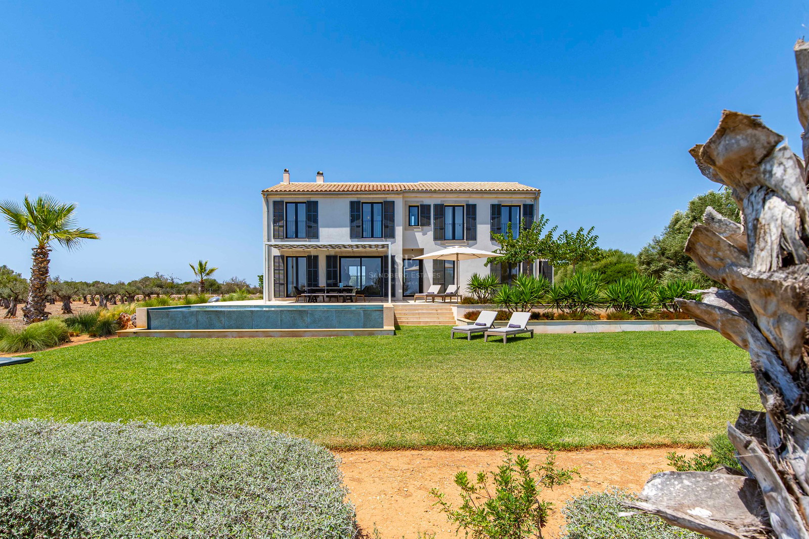 Villa de luxe sur deux étages avec piscine à débordement, pelouse soignée et volets sombres traditionnels.