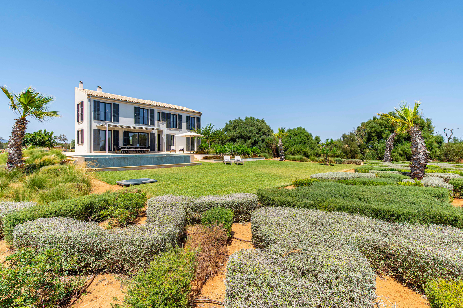 Vue extérieure d'une villa beige de deux étages avec piscine et jardins méditerranéens méticuleusement aménagés.