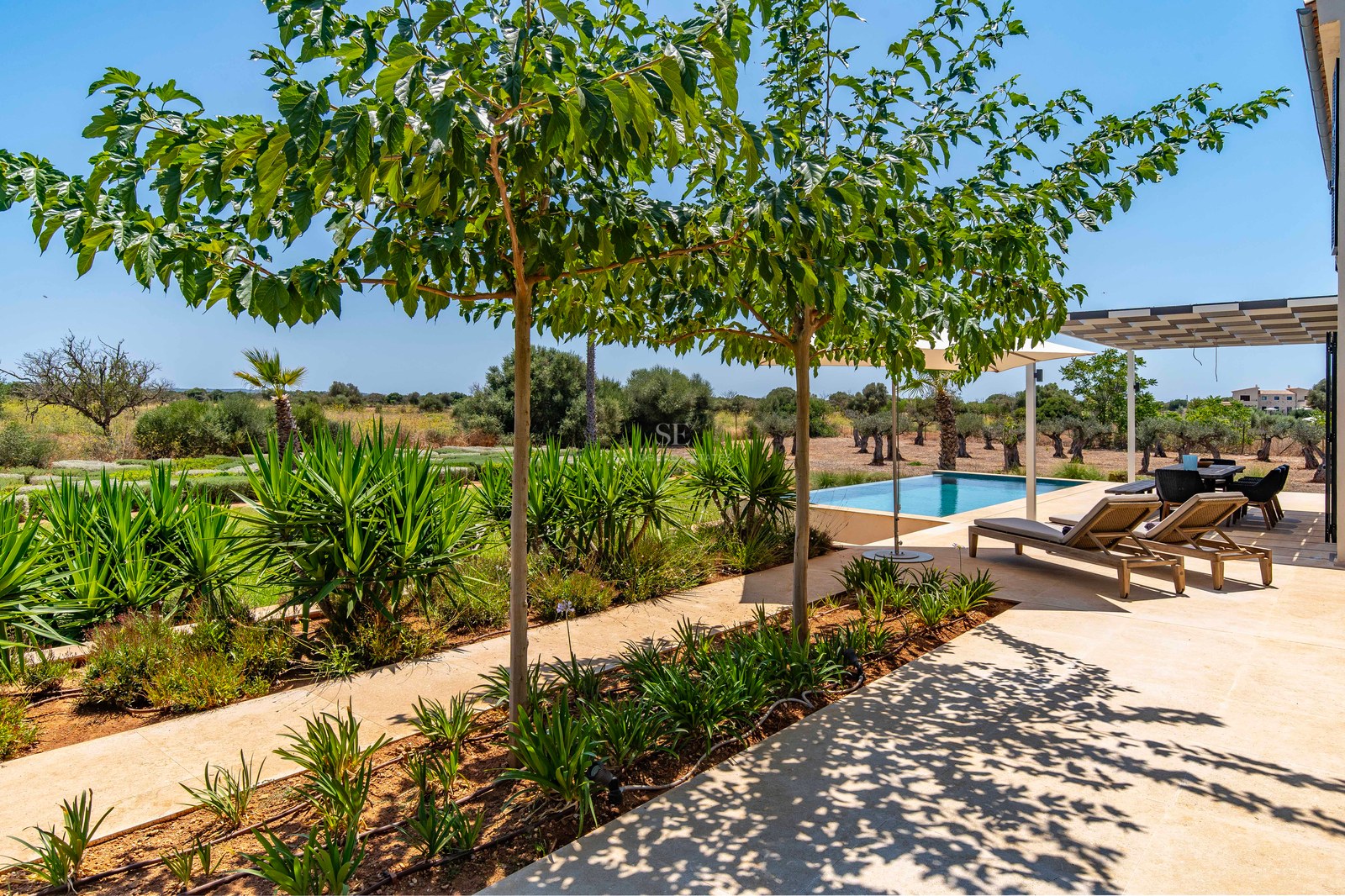 Terrasse en pierre naturelle avec transats au bord d'une piscine, entourée de jardins et de campagne.