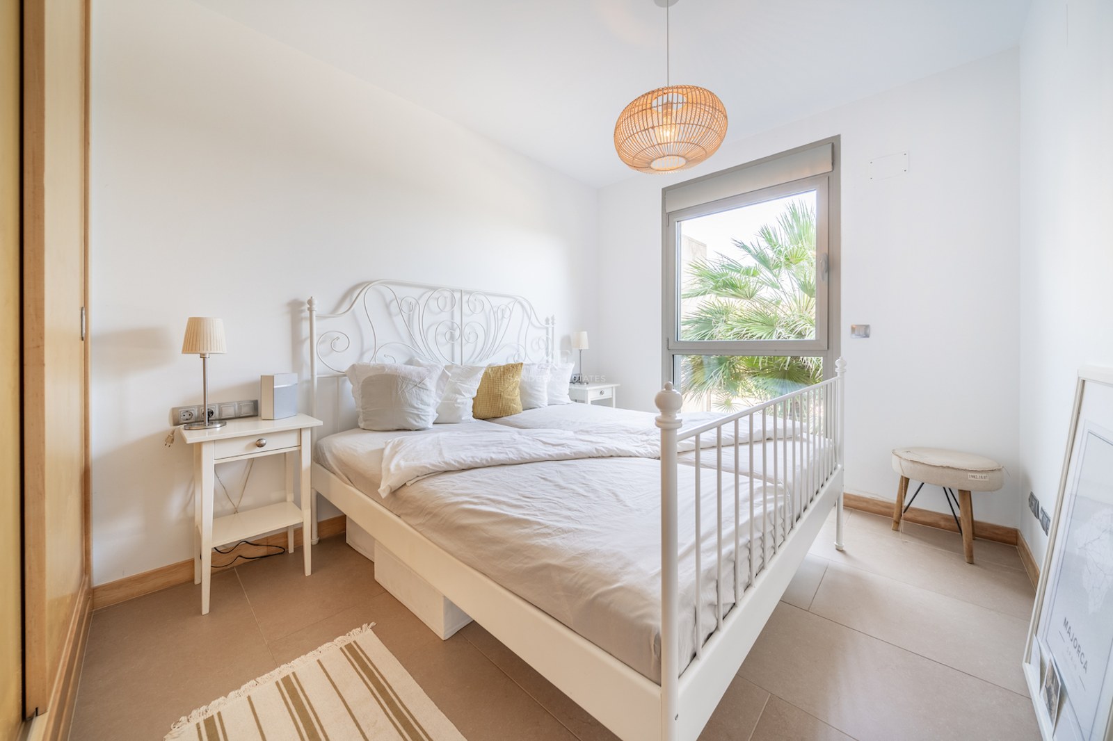 Bedroom featuring a white iron bed, built-in wooden wardrobe, and a window with a palm tree view.