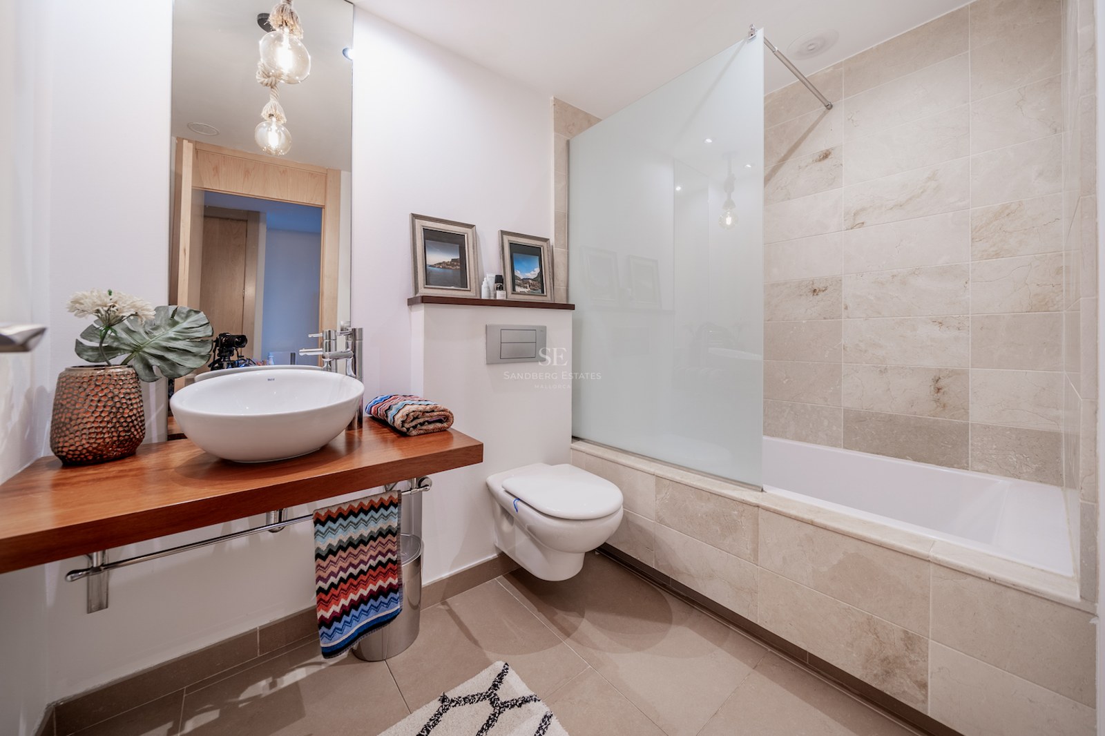 Modern bathroom featuring a wooden vanity, vessel sink, wall-hung toilet, and a bathtub with stone tile walls.