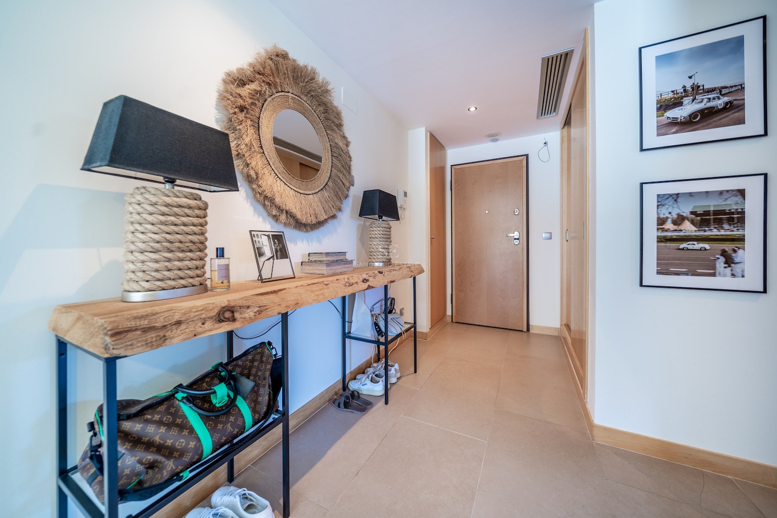 Modern entrance hallway featuring a live-edge wooden console table, round jute mirror, and warm beige tiling.