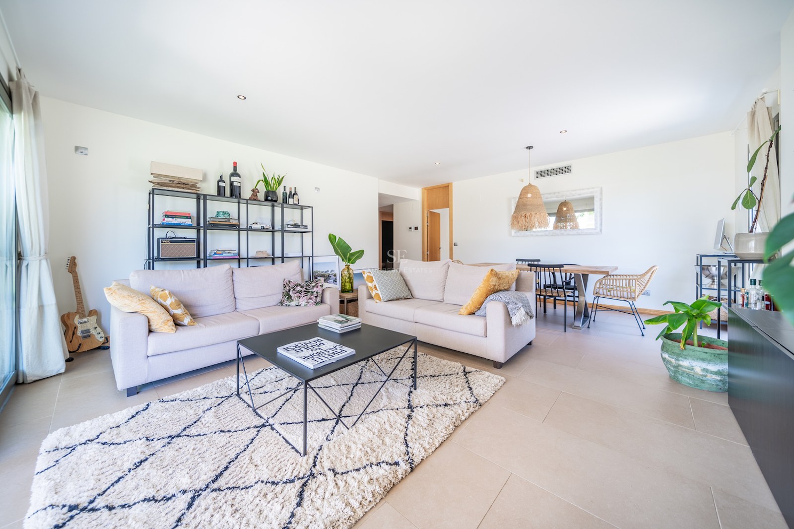 Spacious living room featuring neutral sofas, a geometric wool rug, black metal shelving, and an integrated dining area.