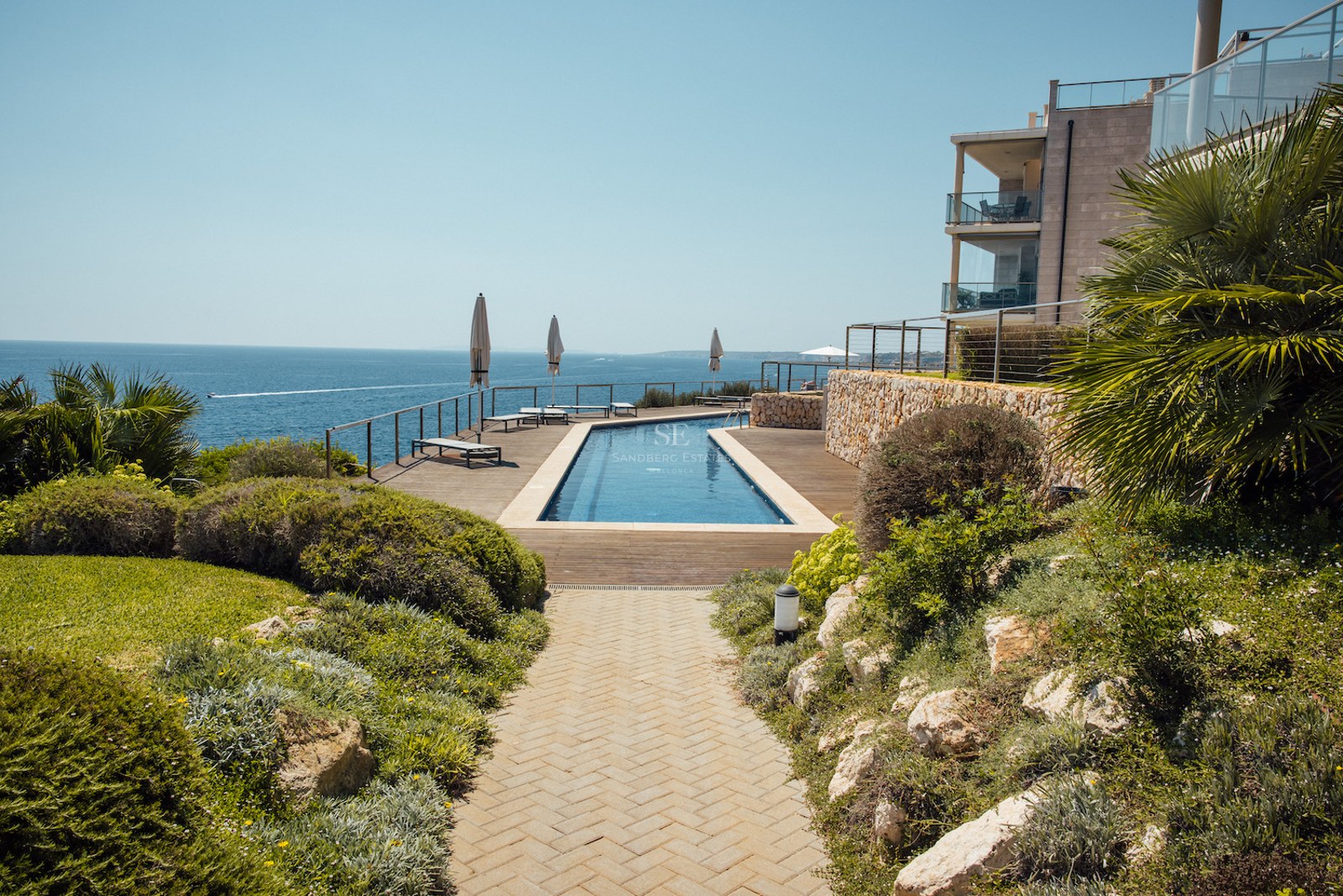 Long rectangular swimming pool on a wooden deck overlooking the Mediterranean sea with landscaped gardens.