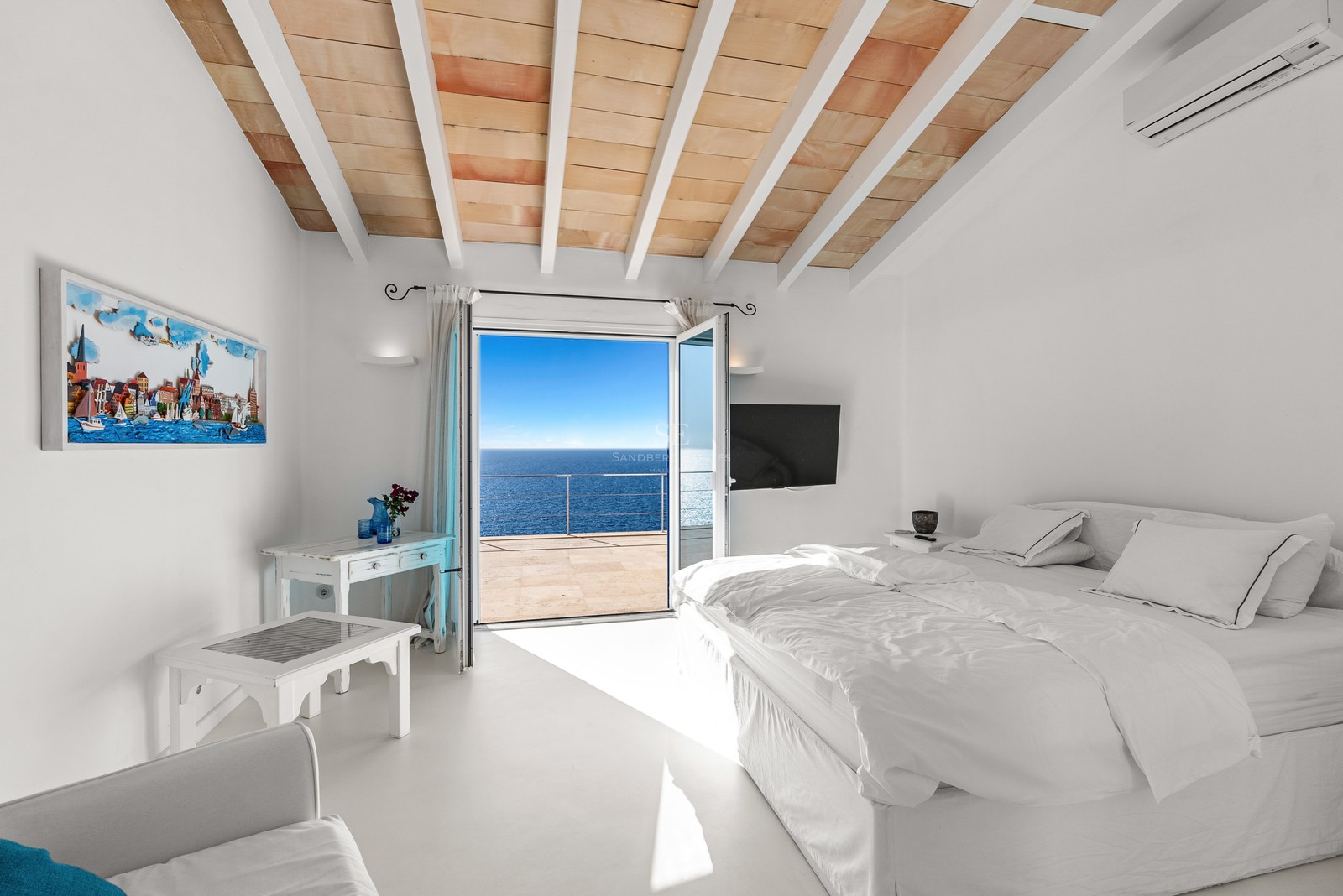 Bright bedroom with white linens, terracotta-tiled ceiling, and open doors leading to a terrace overlooking the blue sea.