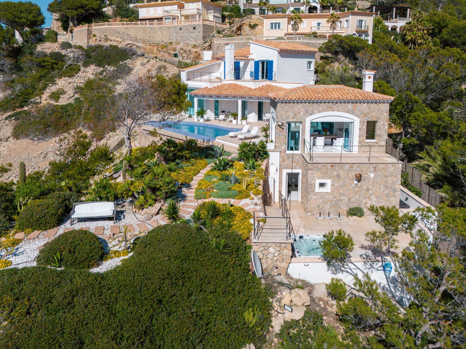 Elevated view of a multi-level stone villa on a hillside featuring an infinity pool and landscaped gardens.