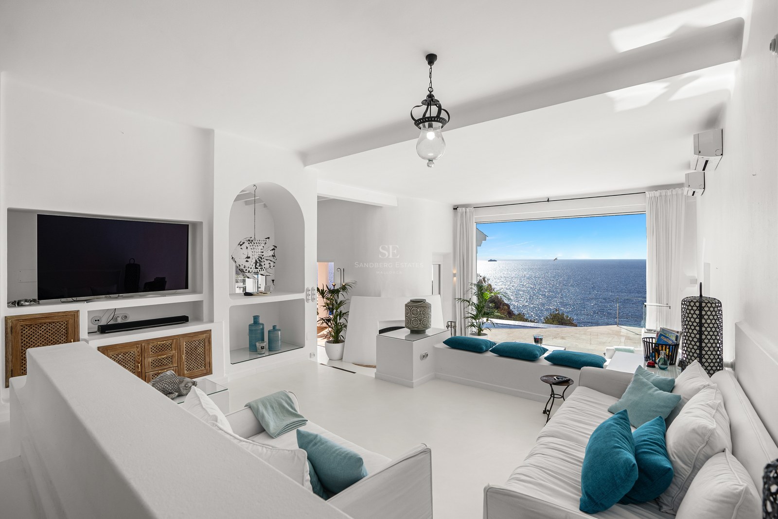 Bright white living room with turquoise cushions and a large window overlooking the sparkling Mediterranean Sea.
